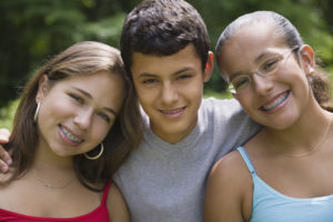 Three preteen siblings smiling outdoors together.