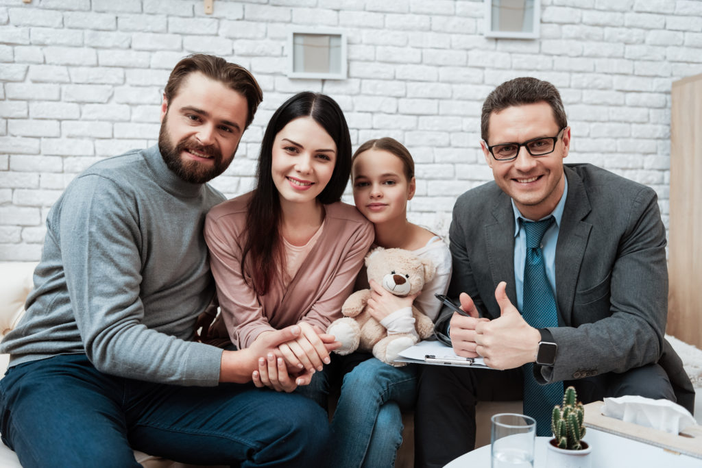 Mother, father, and daughter smiling with therapist in office