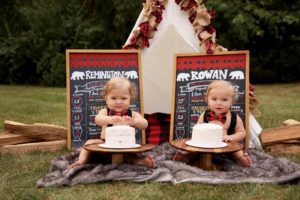 Twin baby boys in bowties celebrate birthday outside with cakes