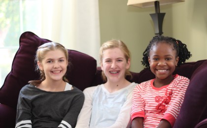 Three young girls smile together as therapeutic foster child enjoys family and siblings