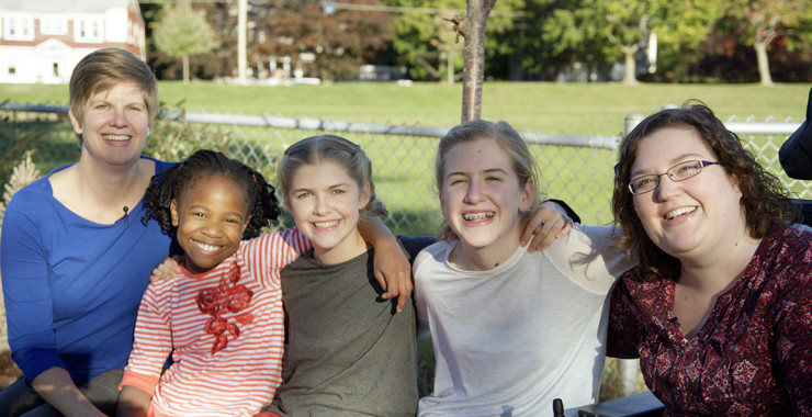 LGBT foster mothers smile with three young girls outdoors