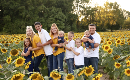Large adopted family celebrates in sunflower field.