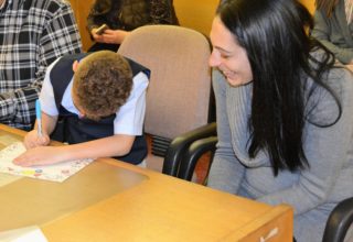 mother beaming at young boy in vest coloring on adoption day in court